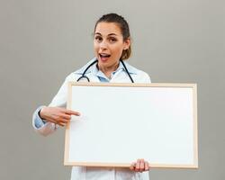 Beautiful female doctor is holding whiteboard on gray background. photo