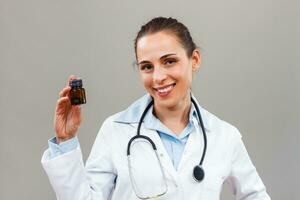 Portrait of beautiful female doctor looking at camera and holding bottle of pills. photo