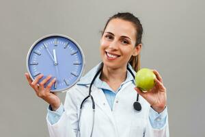 Beautiful female doctor is holding apple and clock photo