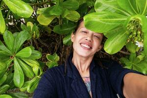 gracioso sonriente mujer tomando selfies entre tropical hojas. foto