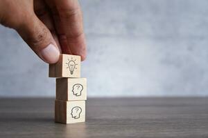 Hand pick wooden cubes with lightbulb icon on top of human head icon. Creative idea, brainstorming and innovation concept. photo