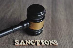 Close up image of judge gavel and text SANCTIONS on wooden table. photo