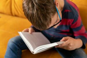 Enraptured Schoolboy in Glasses Absorbed in Reading on the Couch photo