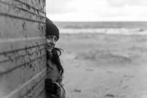 otoño playa serenidad. mujer vistiendo rojo sombrero poses por antiguo cambiando cabina en playa ajuste foto