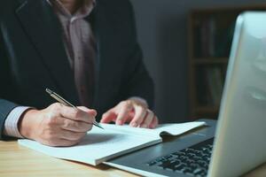 Man using smartphone and taking notes in planning. which is payment online, sits on the chair in the living room at home on a desktop. The concept of finance and online shopping. photo