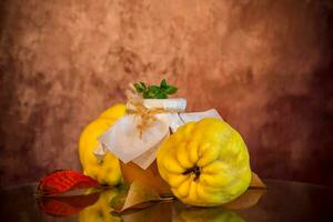 Ripe quince fruits with jam in a glass jar on a dark wooden table. photo