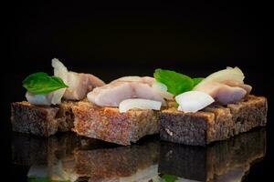 canape of pieces of salted herring with onions on a fresh dark piece of bread. photo
