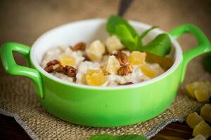 cooked boiled sweet oatmeal with nuts and candied fruits in a bowl photo