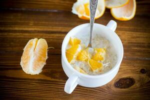 cooked boiled sweet oatmeal with oranges in a bowl photo