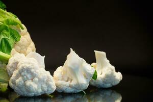 slices of raw small raw cauliflower on black background photo