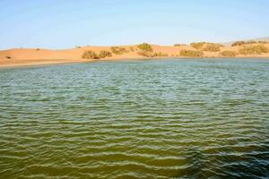 a lake in the desert with sand dunes in the background photo