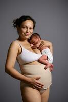 latín americano hermosa cuidando madre, vistiendo un elástico vendaje después cesárea, que lleva su adorable recién nacido bebé foto