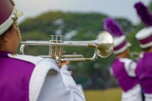 de cerca de estudiantes mano prensado el botón de un trompeta a persecución un musical nota, jugando un canción mientras practicando para un colegio desfile. suave y selectivo enfocar. foto