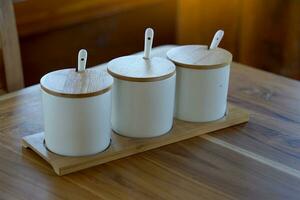 Set of ceramic cups with lids made from wood placed on thedining table for adding condiments such as chili powder, sugar, fish sauce, vinegar with chilli to add flavor to the food. photo