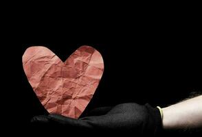 a person holding a crumpled paper heart on a black background photo