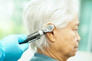 otorrinolaringólogo o ent médico médico examinando mayor paciente oído con otoscopio, escuchando pérdida problema. foto