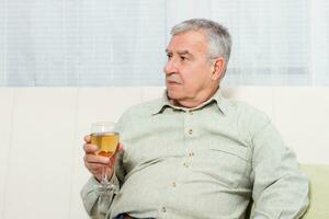 Sad senior man sitting on the sofa and drinking wine. photo