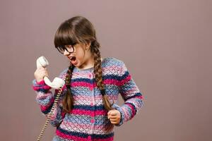 pequeño nerd niña es gritos a el teléfono foto