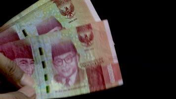 räkning 100 000 rupiah förbi hand på svart bakgrund. indonesiska valuta, betyder av betalning i indonesien video