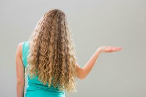 Woman with gorgeous long blonde hair gesturing on gray background. photo