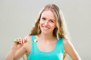 hermosa joven mujer cepillado dientes en gris antecedentes. foto