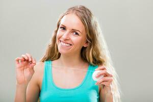 hermosa joven mujer utilizando dental seda floja en gris antecedentes. foto