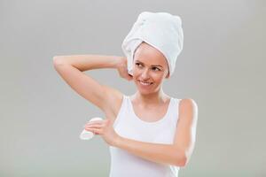 Beautiful young woman applying antiperspirant on gray background. photo