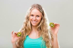 Beautiful young woman showing slices of kiwi on gray background. photo