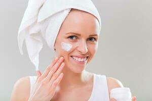 Beautiful young woman applying moisturizer on gray background. photo