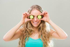 Beautiful young woman showing slices of cucumber on gray background. photo