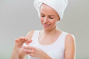 Beautiful young woman using moisturizer on gray background. photo