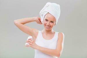Beautiful young woman applying antiperspirant on gray background. photo