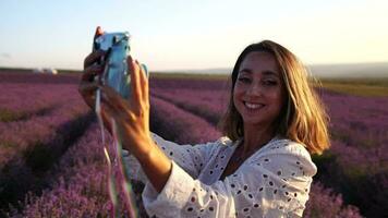 glimlachen gelukkig vrouw fotograferen met ogenblik camera in lavendel veld- Aan zonnig dag. jong vrouw het schieten met blauw ogenblik camera modieus meisje nemen selfie buitenshuis video