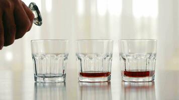 een man's hand- giet alcohol in een glas. dichtbij omhoog. drie bril met alcohol, whisky is toegevoegd naar een van hen video