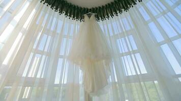 The bride's luxurious wedding dress hangs on the panoramic glass. The morning of the wedding day. White wedding dress video