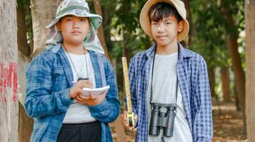 Young Asian boys are using a measure tape to measure a tree in a local park, soft and selective focus photo