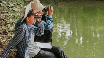 joven asiático Niños son utilizando un binocular a Estar atento para aves y animales en un local parque, suave y selectivo atención foto