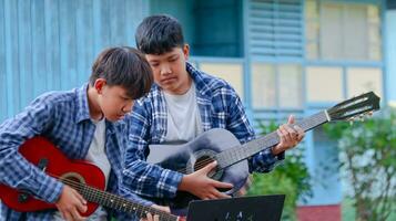 joven asiático Niños son jugando acústico guitarras en frente de un casa concepto de aprendizaje y gratis hora ocupaciones foto