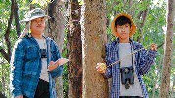 Young Asian boys are using a measure tape to measure a tree in a local park, soft and selective focus photo