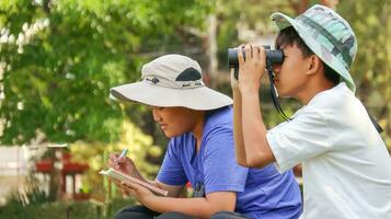 joven asiático Niños son utilizando un binocular a Estar atento para aves y animales en un local parque, suave y selectivo atención foto