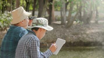 joven asiático Niños son utilizando un binocular a Estar atento para aves y animales en un local parque, suave y selectivo atención foto