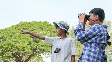 Young Asian boy is using a binocular to lookout for birds and animals in a local park, soft and selective focus photo