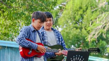 joven asiático Niños son jugando acústico guitarras en frente de un casa concepto de aprendizaje y gratis hora ocupaciones foto