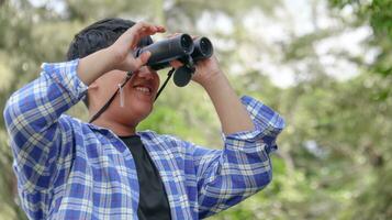 joven asiático chico es utilizando un binocular a Estar atento para aves y animales en un local parque, suave y selectivo atención foto