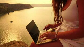 Woman laptop sea. Happy successful woman, female freelancer typing on computer by the sea at sunset, makes a business transaction online from a distance. Freelance, remote work on vacation. Close up video