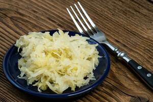 Homemade pickled sauerkraut in a bowl with a fork on a wooden board photo