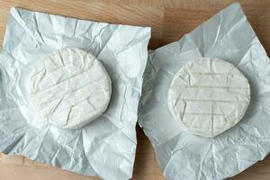 dos cabezas de queso camembert sobre papel blanco en la tabla de cortar. preparación para asar a la parrilla foto
