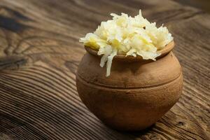 Homemade pickled sauerkraut in a ceramic jar on a wooden board photo