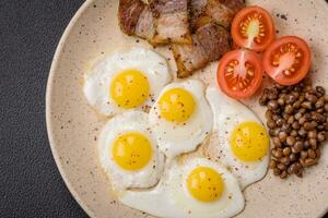 Delicious nutritious breakfast of fried quail eggs, bacon, legumes and cherry tomatoes photo