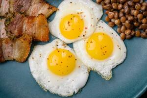 Delicious nutritious breakfast of fried quail eggs, bacon, legumes and cherry tomatoes photo